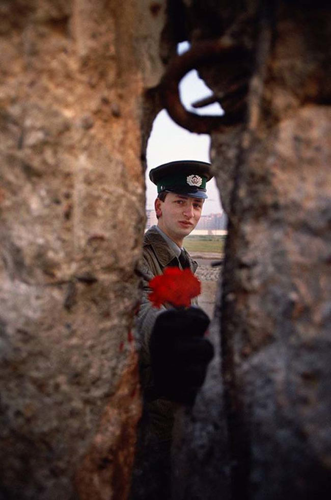 33 - 1989 - East German soldier passing a flower through the Berlin Wall before it was torn down